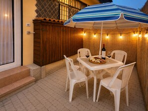 An outdoor patio with a table set for two, a bottle of wine, and a plate of cheese and cured meats.