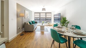 Ein modernes Wohnzimmer mit einer Couch, einem Couchtisch und einem Essbereich mit Stühlen und einem für eine Mahlzeit gedecktem Tisch.