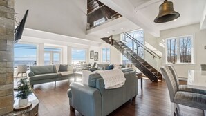 A spacious living area with a high ceiling, a staircase, and a large window offering a view of the outdoors. - The Vista Del Mar 596 (Hubbards)