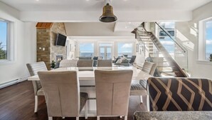 A spacious living area with a dining table, comfortable seating, a fireplace, and a staircase leading to an upper level. - The Vista Del Mar 596 (Hubbards)