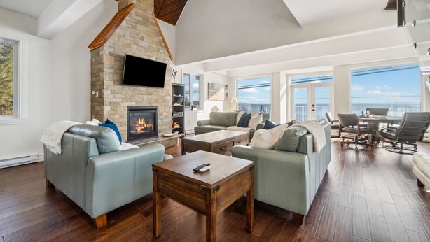 A spacious living room with a stone fireplace, comfortable seating, a flat-screen TV, and a view of the ocean. - The Vista Del Mar 596 (Hubbards)