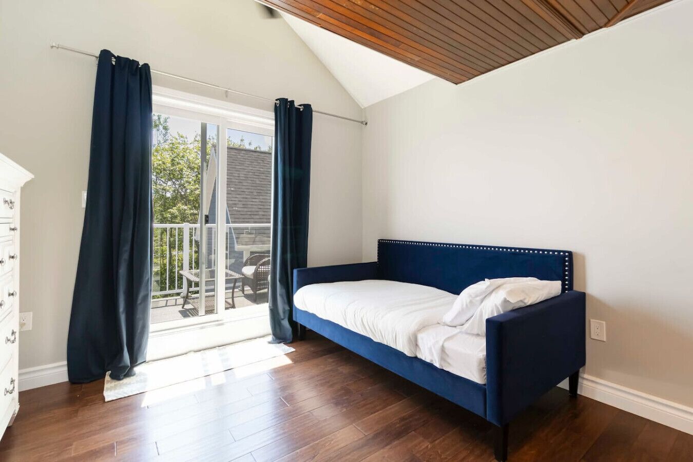 Une chambre avec un lit simple, un balcon avec une chaise et un plafond en bois.