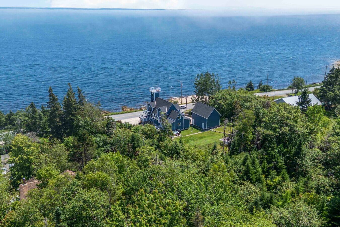 A coastal house with a large water tank, surrounded by dense greenery and a view of the sea.
