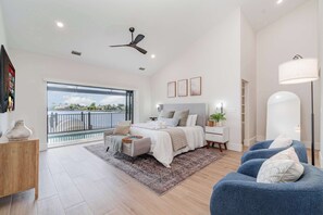 A bedroom with a large window, a bed, a desk, a chair, and a balcony. - New Remodel! Pool, Spa & Tiki | Thunderbird Lake (Cape Coral)