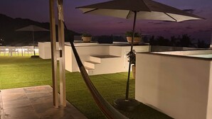 En tagterrasse med hængekøje, udendørs møbler og udsigt til bjergene i skumringen.