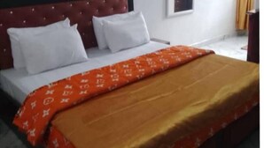 Ein Hotelzimmer mit Bett, weißen Kissen, einer roten Kopfteil, einer Klimaanlage, einem Fenster mit Vorhängen und einem kleinen Tisch.