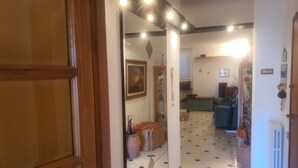 Un corridoio con pavimento piastrellato, una porta in legno e uno specchio che riflette una zona cucina con lavello, fornelli e pensili.