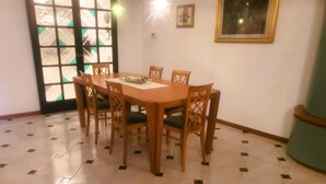 Un'area pranzo con un tavolo e sedie in legno, pavimento piastrellato, una porta con pannelli di vetro e un quadro appeso al muro.