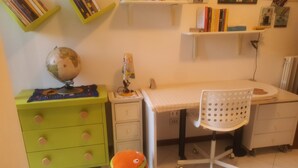 Una cameretta con scrivania, sedia, mappamondo e un piccolo giocattolo arancione.