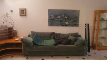 Un soggiorno con un divano verde, un quadro appeso al muro, un mobile contenitore e un pavimento piastrellato.