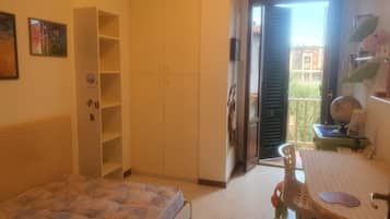 Une chambre à coucher comprenant un lit, une armoire, un bureau avec une chaise et une porte-fenêtre donnant sur un balcon.