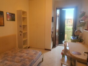Ein Schlafzimmer mit einem Bett, einem Kleiderschrank, einem Schreibtisch mit Stuhl und einer Balkontür.