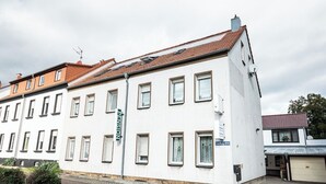 A white building with multiple windows and a red-tiled roof. - Pension Greiser: Affordable accommodation in Leipzig (Leipzig)