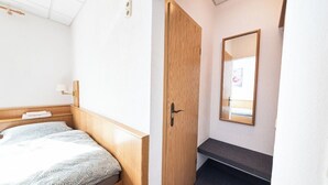 A hotel room with a bed, a wooden door, a mirror, and a small bench. - Pension Greiser: Affordable accommodation in Leipzig (Leipzig)