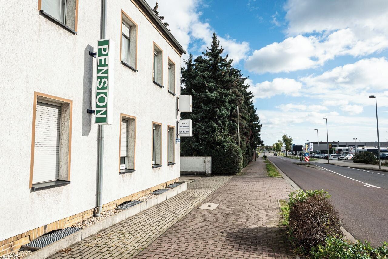 A building with a 'PENSION' sign, a paved sidewalk, and a street with vehicles.