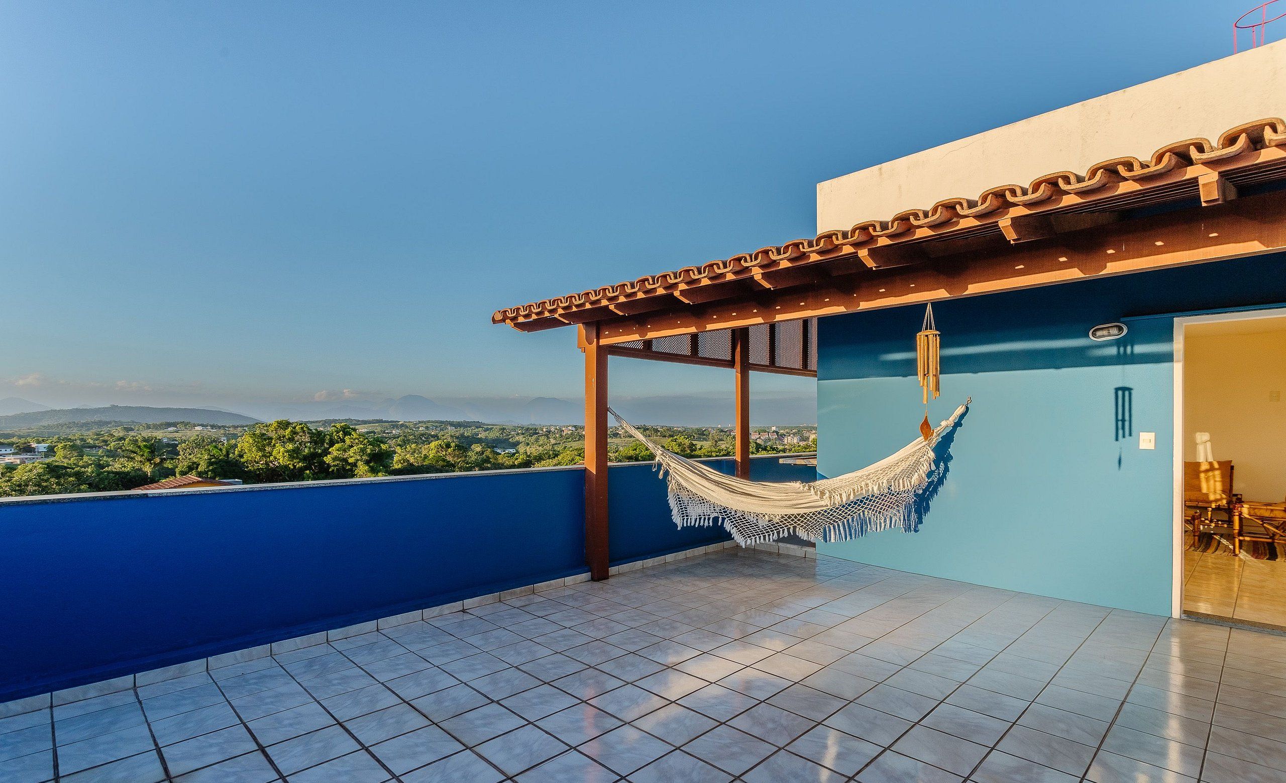 A rooftop terrace with a hammock, blue walls, and a view of the landscape.