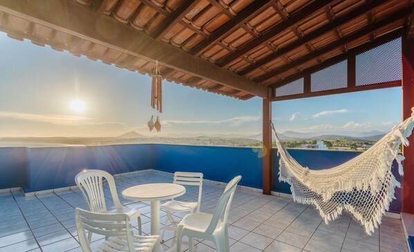Une terrasse avec un hamac, des chaises en plastique blanches et une table.