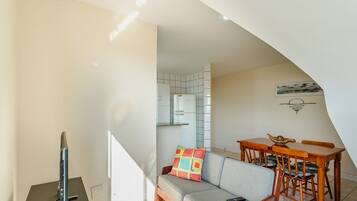 Uma sala de estar moderna com um sofá, uma mesa de jantar de madeira e cadeiras. Uma televisão está posicionada sobre um suporte.