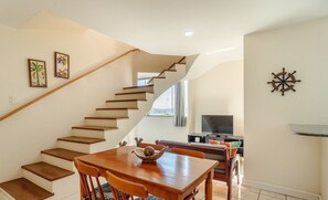 Un intérieur moderne avec un escalier en bois, un coin repas comprenant une table et des chaises en bois, un téléviseur et un élément décoratif en forme de roue de voilier.