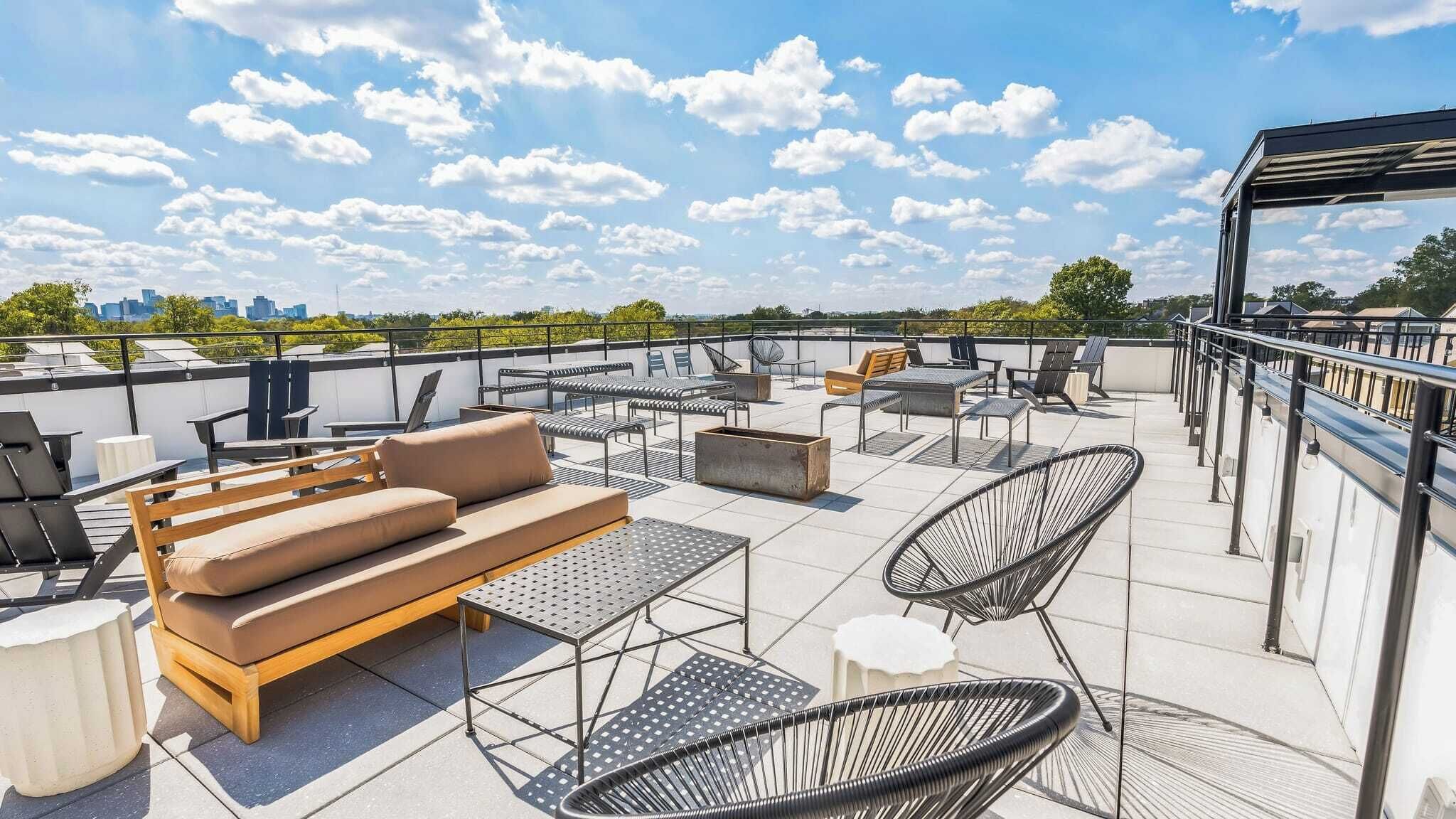 Una terraza en la azotea con mobiliario exterior, incluyendo un sofá, sillas y mesas, y vistas al horizonte de la ciudad.