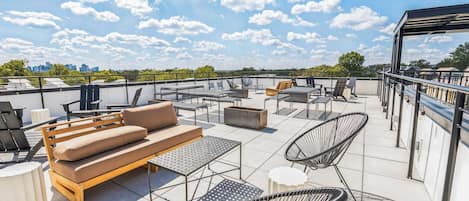 Una terraza en la azotea con mobiliario exterior, incluyendo un sofá, sillas y mesas, y vistas al horizonte de la ciudad.