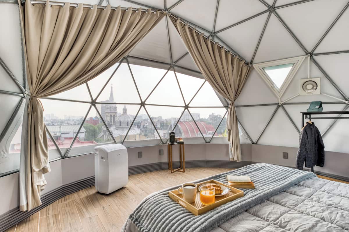 A room with a large window, a bed, a tray with breakfast items, and a view of a cityscape.