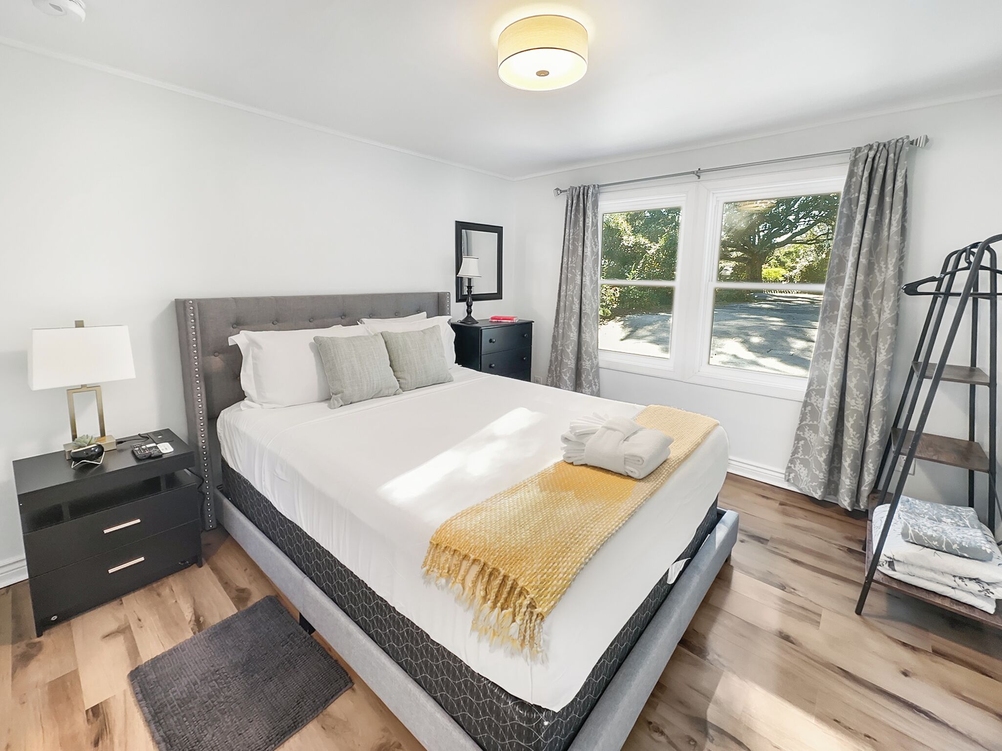 Una camera da letto moderna con un letto grande, comodini, un tavolino e una finestra con tende, con vista su spazi verdi.