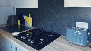 A kitchen with a black stove, a toaster, and a wall-mounted knife holder. - 2 bed Holiday Let-Contractors -Parking-Nr to hospital, Uni, City Centre, stadium (Sunderland)