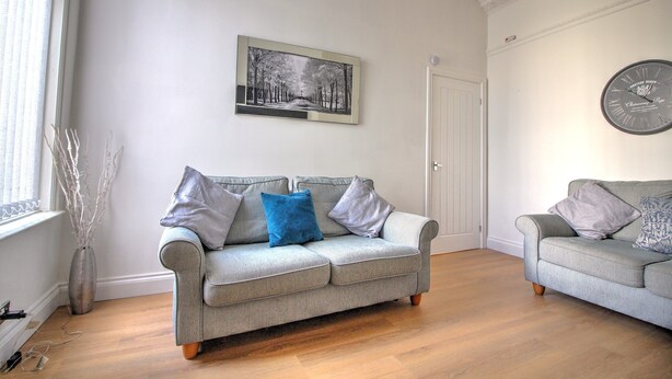 A living room with two grey sofas, a framed black and white photo on the wall, and a clock. - 2 bed Holiday Let-Contractors -Parking-Nr to hospital, Uni, City Centre, stadium (Sunderland)