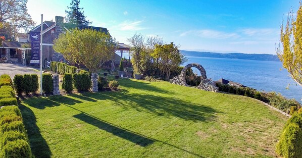 Un césped bien cuidado, un sendero de piedra y un arco de piedra que conduce a un edificio con un letrero que dice 'Camano Island Cuisine', ofreciendo comida, cerveza y vino.