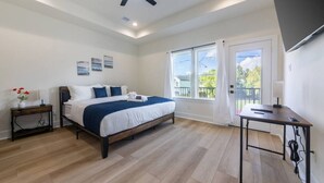 A modern bedroom with a bed, bedside tables, a desk, and a balcony with a view.