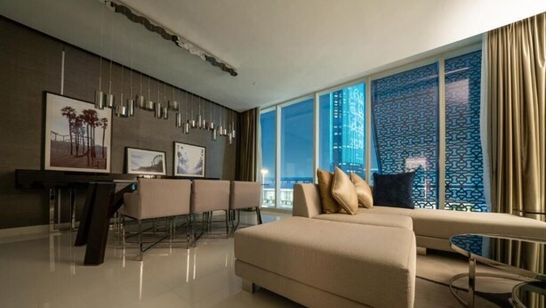 A modern living room with a sofa, a coffee table, and a dining area with chairs and a table. - DAMAC Super Luxury Two Bedroom Apartment (Riyadh)