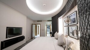A modern hotel room with a large bed, a flat-screen TV mounted on the wall, a ceiling light, and a view of the hallway. - DAMAC Super Luxury Two Bedroom Apartment (Riyadh)
