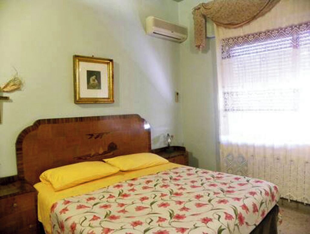 A bedroom with a wooden bed, yellow pillows, a framed picture on the wall, and a window with curtains.