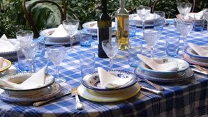 A table set outdoors with a checkered tablecloth, plates, glasses, and a bottle of wine.