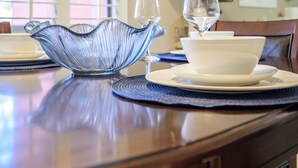 Une table à manger dressée avec un pichet en verre bleu, des verres à vin et des assiettes blanches.
