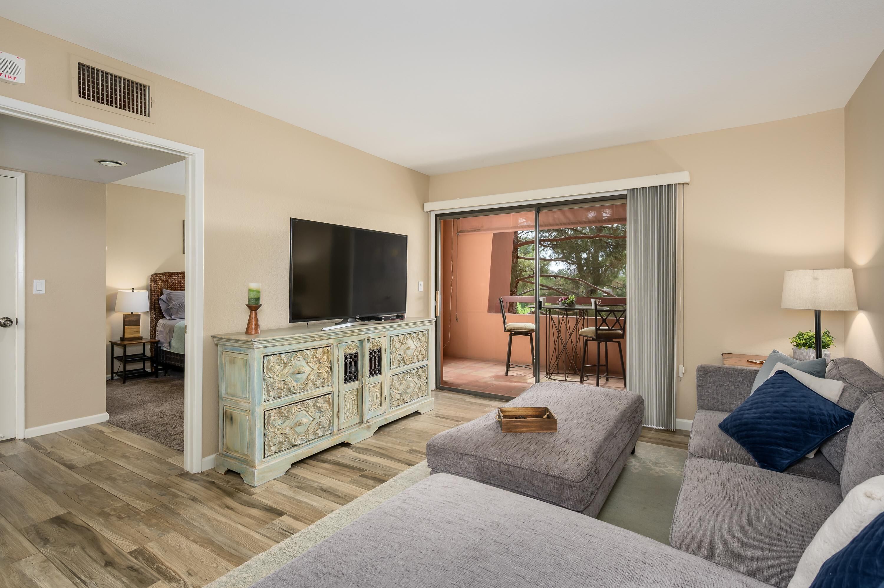 A living room with a television, a sofa, a cabinet, and a balcony with a table and chairs.