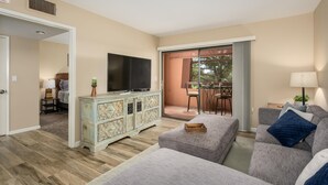 Un salon comprenant un téléviseur, un canapé, un meuble et un balcon avec une table et des chaises.