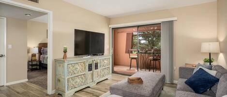 A living room with a television, a sofa, a cabinet, and a balcony with a table and chairs.