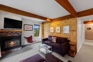 A modern living room with a fireplace, a flat-screen TV, a red chair, a brown sofa, and a wooden wall with framed pictures.