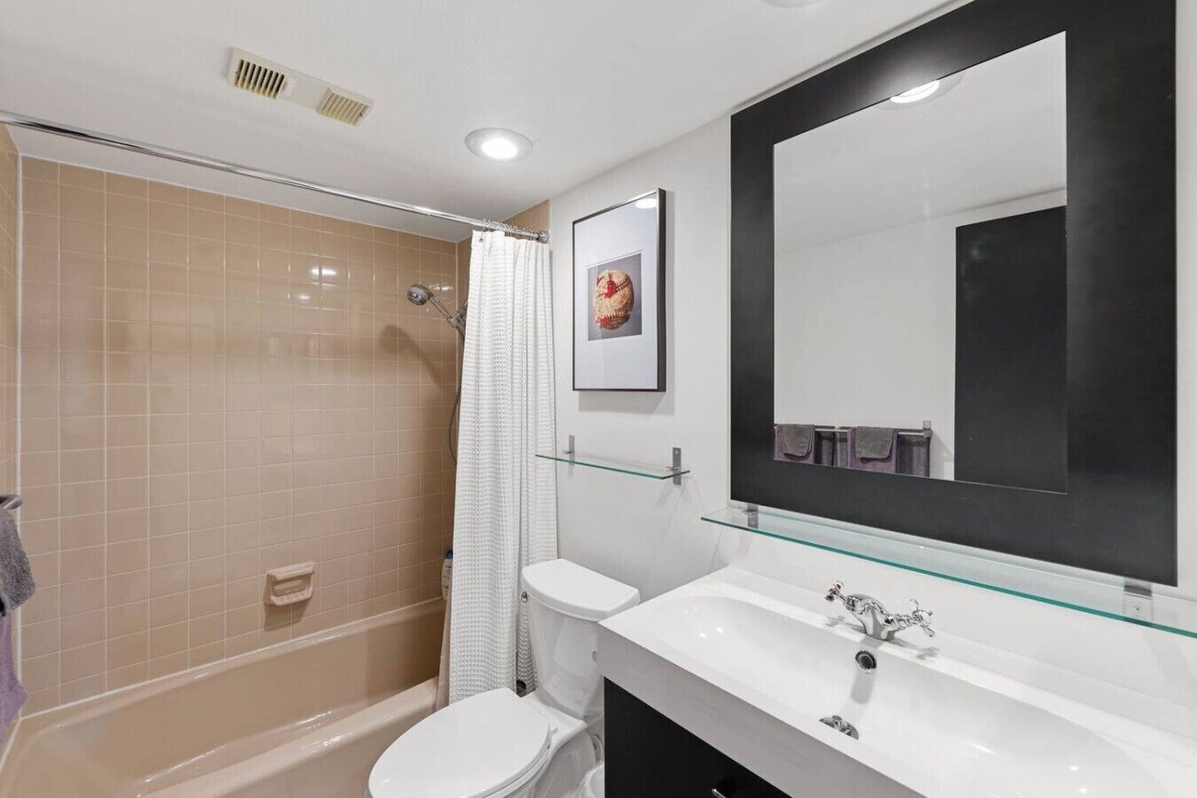 Une salle de bain avec une douche, des toilettes et un grand miroir au-dessus d’une étagère en verre.