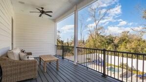 Eine überdachte Veranda mit einem Korbsessel, einem Holztisch und einem Deckenventilator.