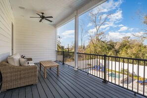 A covered porch with a wicker sofa, a wooden table, and a ceiling fan. - Beach Oasis Sleeps 26 Walk to Beach and Private Pool (North Myrtle Beach)