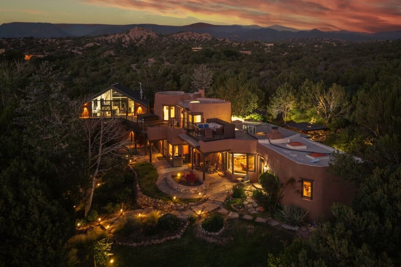 A large, modern house with multiple levels, large windows, and a well-lit outdoor area.