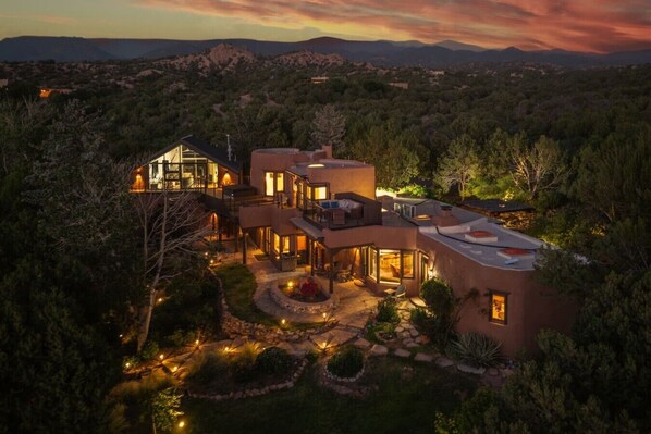 A large, modern house with multiple levels, large windows, and a well-lit outdoor area.