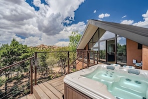 A modern outdoor hot tub area with a wooden deck, a metal railing, and a clear view of the surrounding landscape.