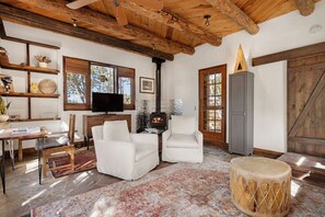 Un interior rústico con chimenea, vigas de madera, televisión y comedor.