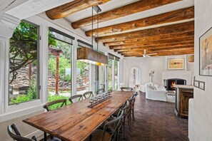 A dining area with a wooden table and chairs, large windows, a fireplace, and a stone wall outside.