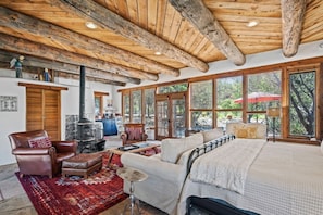 A rustic interior with a wooden ceiling, large windows, a fireplace, and a cozy seating area.