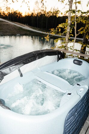 Ein Whirlpool mit schwarzem Deckel, umgeben von Wasser und Bäumen.